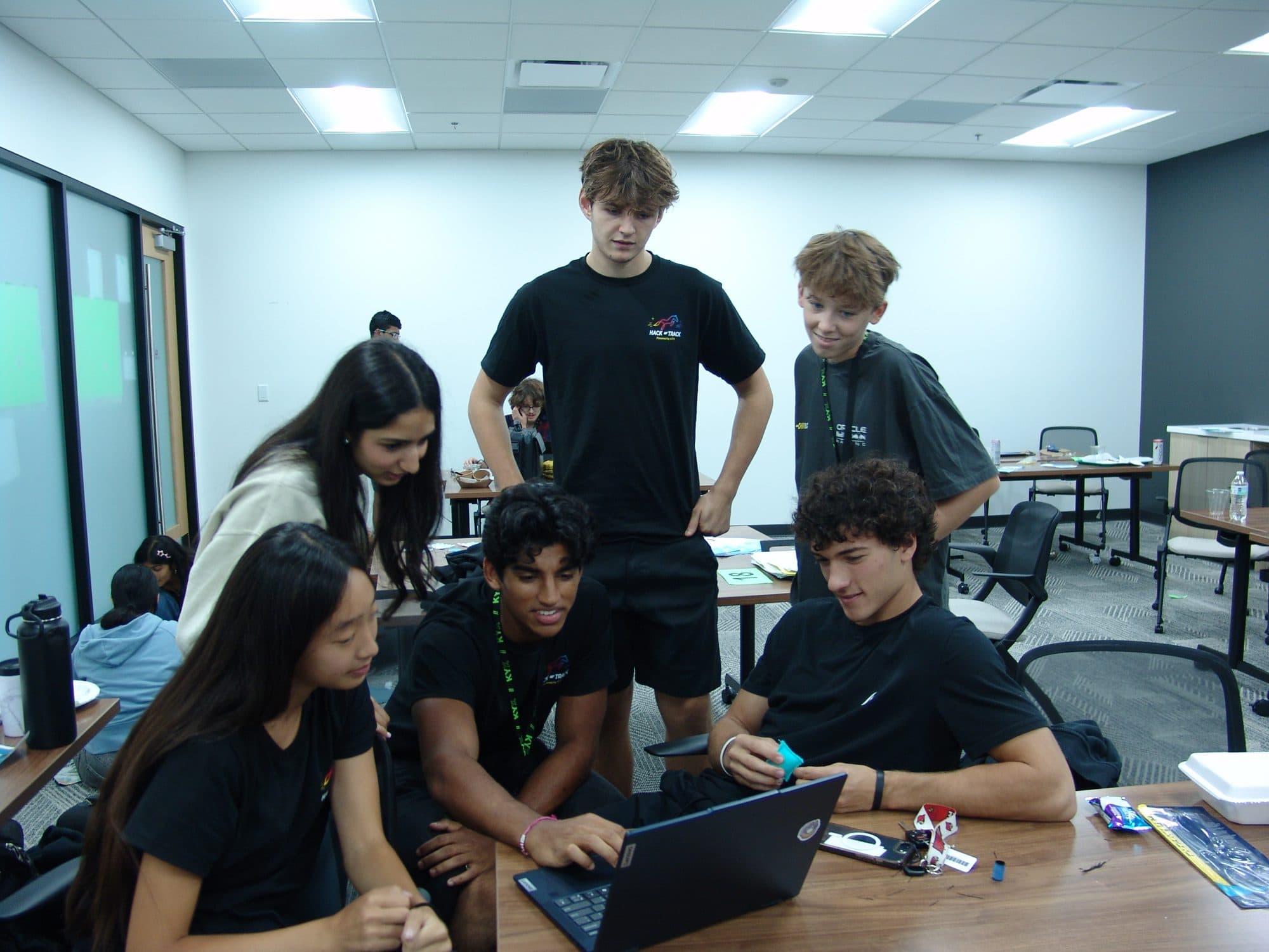 Hack the Track organizers gathered around a team's laptop to help during the Saturday hacking session
