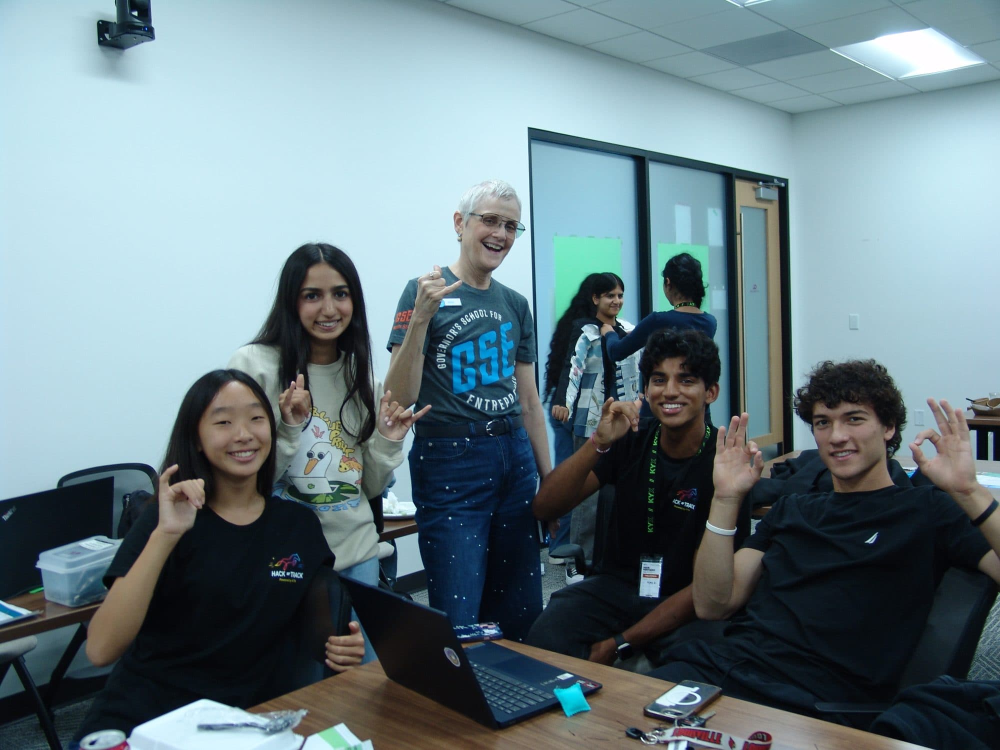 A team and their mentor flashing OK signs at their table during Hack the Track 2026