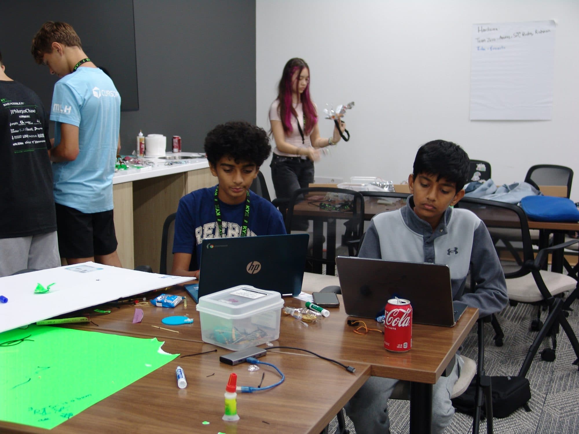 Teams working on laptops and prototypes at Hack the Track 2026, with a hardware project taking shape in the foreground